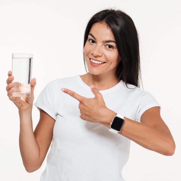 Portrait of a smiling fit woman pointing finger at glass with water and looking at camera isolated over white background